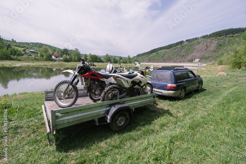 Auto trailer with motocross motorcycles near the river on  summer day