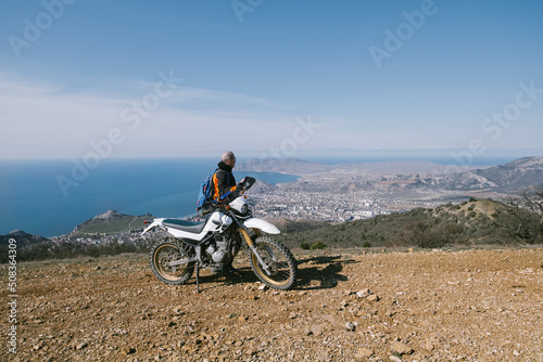Active elderly man riding dirt motorcycle in beautiful mountains hills with city on sea shore landscape