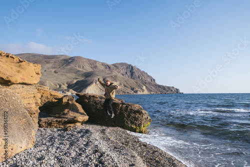 Female resting on the shore of cold blue sea, jumping from stone to the shore. Spring time, cold coast wind