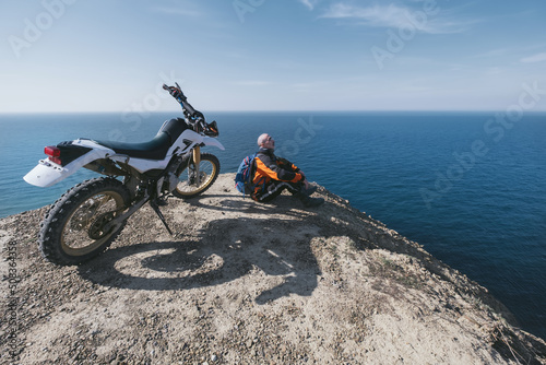 Canvastavla Active elderly man resting near dirt motorcycle on beautiful clff top, sea lands