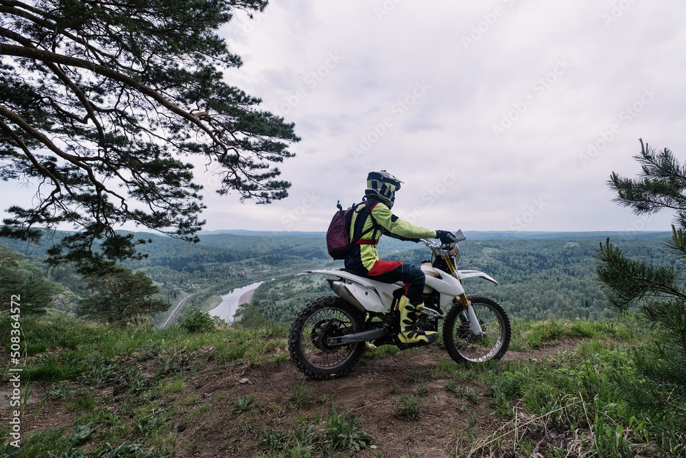 biker resting on enduro motorcycle on the edge of cliff with gorgeous view of mountain skyline