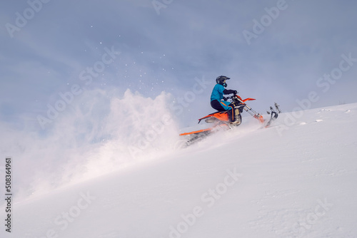 Biker riding snowbike on hillside. Splashes of snow behind motorcycle