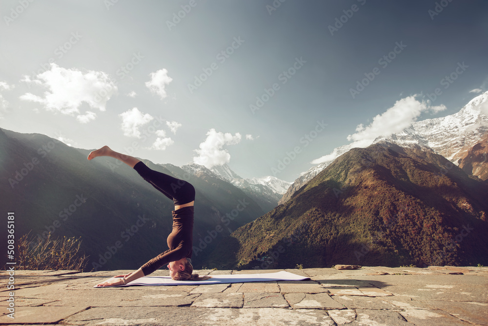 Beautiful yoga picture in magnificent mountain scenery on  sunny day. Yoga outdoor. Young female doing headstand