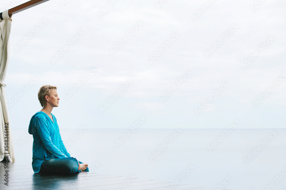 Meditation on sea shore, space for text on photo. Calm female sitting in gazebo meditating and relaxing near water skyline