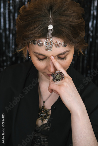 Close up portrait of Tired thoughtful beautiful woman wearing jewellery lowered her gaze and touched forehead with finger