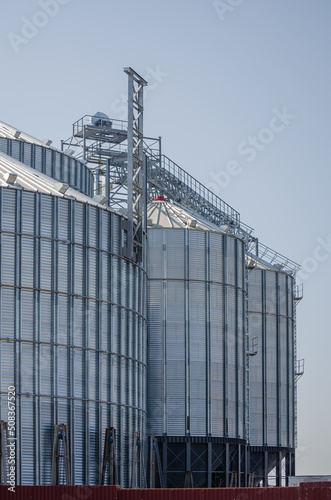 Construction of new cylindrical silos for grain storage. Metal silos are made of corrugated metal. A row of hand winches lifts the metal structure upward. Agribusiness. Grain exports.