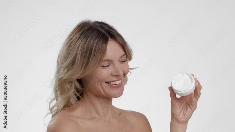 Luxury anti aging cosmetics. Happy beautiful middle aged lady demonstrating organic cream jar, white studio background Luxury anti aging cosmetics. Happy beautiful middle aged lady demonstrating organic cream jar, white studio background