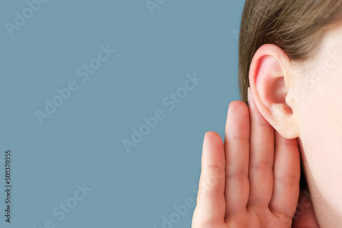 The girl listens attentively with her palm to her ear close-up, the news concept