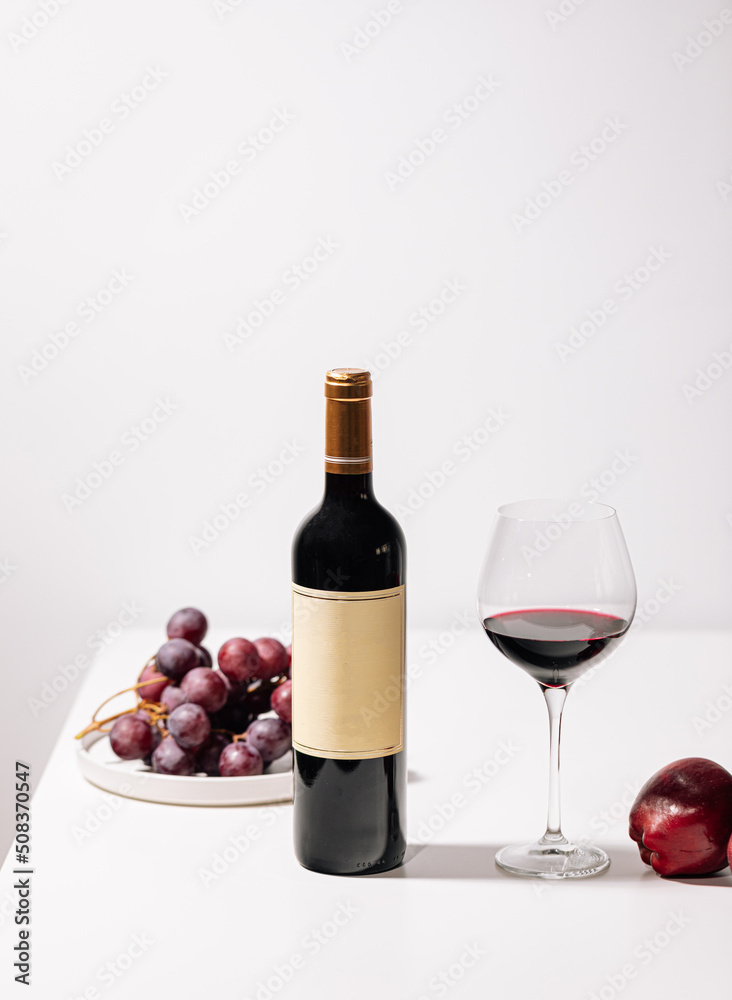 Obraz premium Glass of red wine with grapes and apples on white table