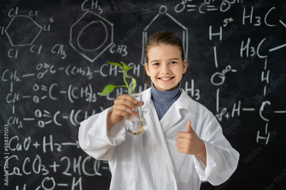 Young student holding a small plant in a flask at elementary sciences lesson, little scientist in a biolab growing a sprout, science and school education