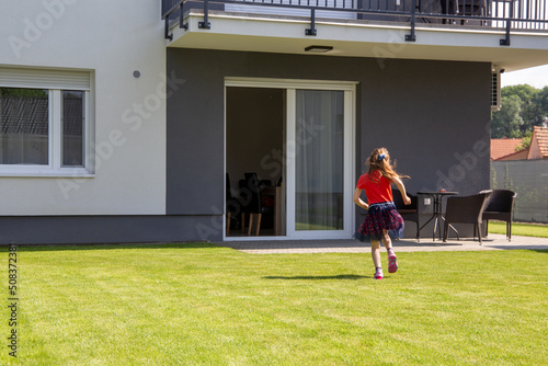 Symbolbild Wohnen und Familienidylle: Mädchen im Garten eines neu gebauten Einfamilienhauses (model released)