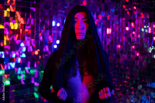 Close-up portrait of an androgenic model in a hood. Male transgender in studio with neon light.