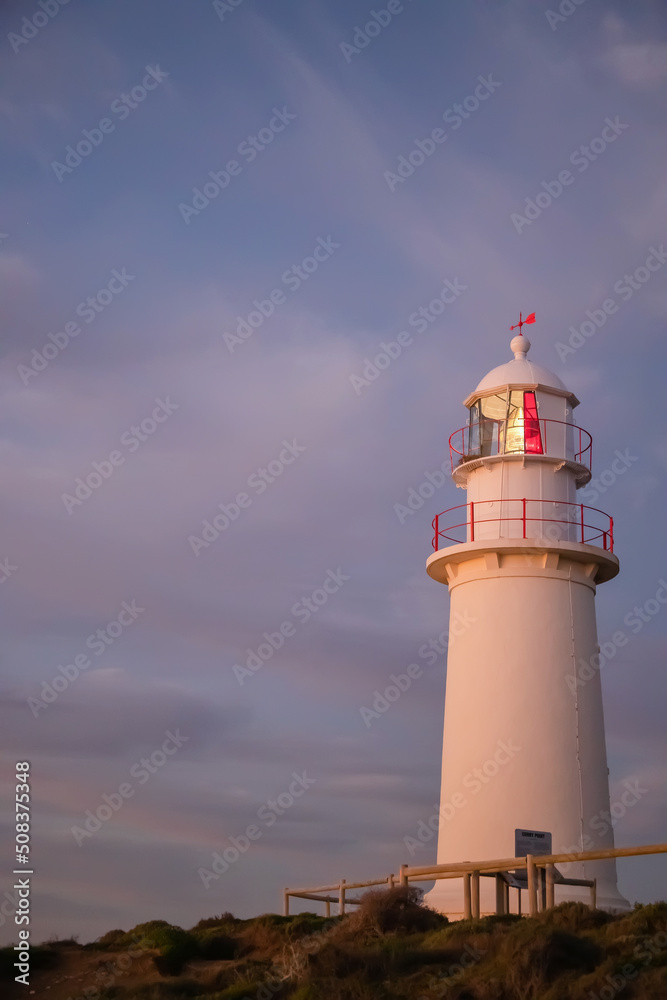 White lighthouse with red elements against the backdrop of the dark blue sunset sky, close up