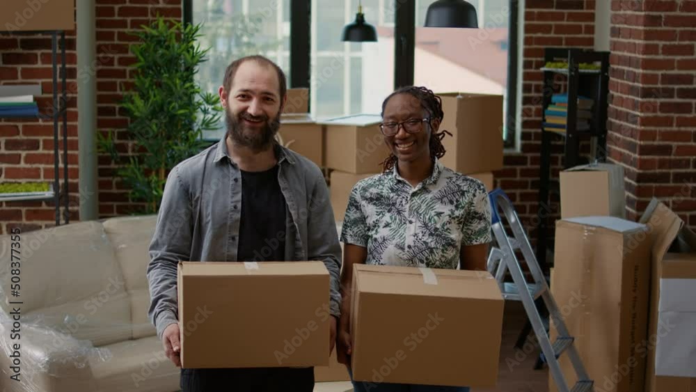 Portrait of husband and african american wife moving in together in new rented apartment flat. Holding cardboard boxes to unpack and prepare real estate property for relocation, household mortgage. Portrait of husband and african american wife moving in together in new rented apartment flat. Holding cardboard boxes to unpack and prepare real estate property for relocation, household mortgage.