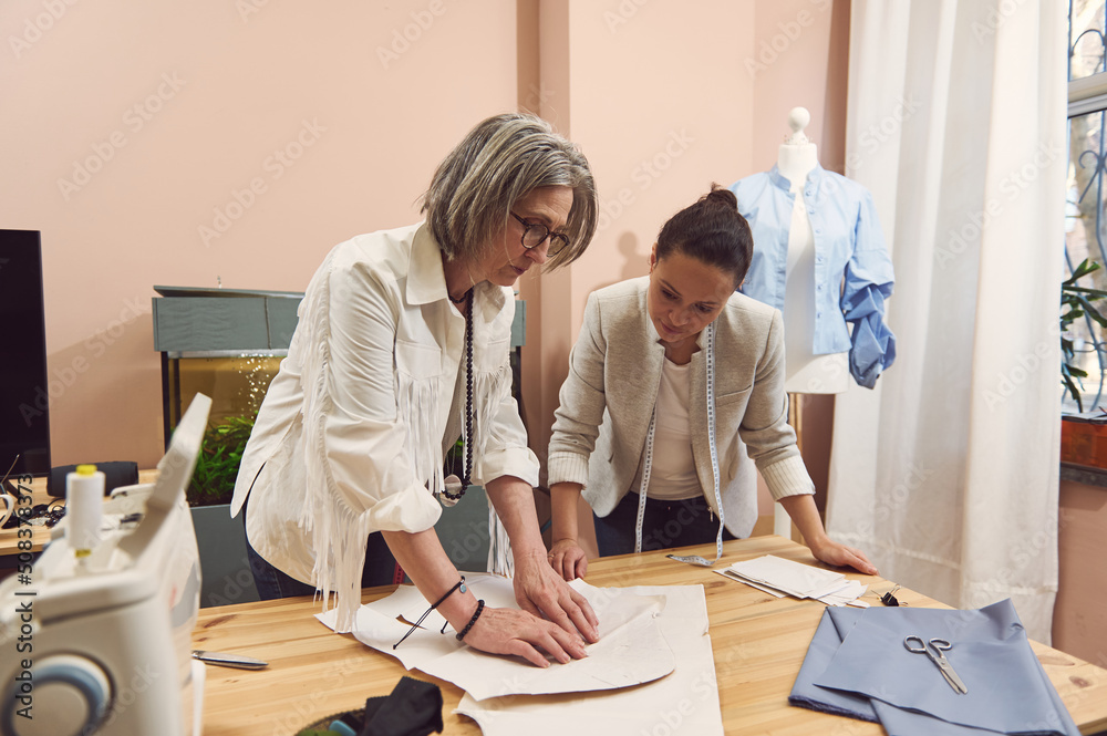 Obraz premium Fashion designers create new fashionable styles, discuss patterns, during the development of a new collection of handmade clothes in a fashion design and tailoring atelier