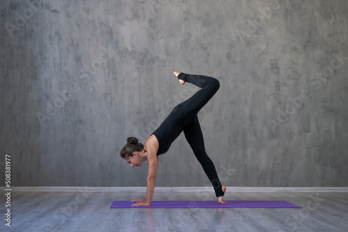 Caucasian young cool attractive yoga woman practicing yoga concept, standing in exercise in workout pose, wearing sports bra and pants, full length against gray wall