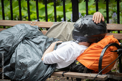 homme sans domicile qui dort sur un banc avec un vieux casque de moto sur la tête et une bâche comme couverture. Illustration de la misère et de la crise économique