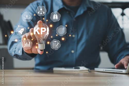 The man is holding light bulb. Key Performance Indicator (KPI) using Business Intelligence (BI) metrics to measure achievement versus planned target, person touching screen icon, success.