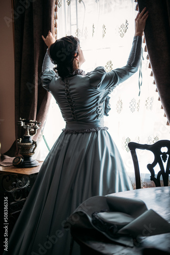 Fotografija Beautiful woman in blue vintage 1800s early 1900s clothing Cottagecore Edwardian Victorian Epoque dress in old interior