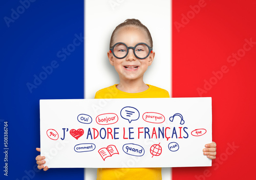 Beautiful cute little girl holding a white board with i love French text and illustrations in front of blurry flag of France. English: I Love French. photo