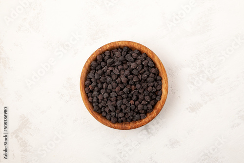 Black chickpeas in wooden bowl on light grey texured background, close-up. Selective focus, copy space