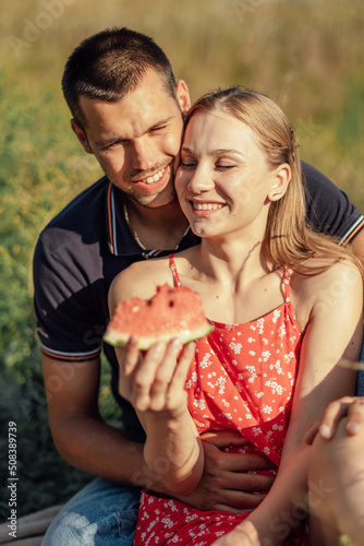 Young couple in love on summer picnic with watermelon. Loving couple sitting by the river, talking, smiling, laughing, eating watermelon