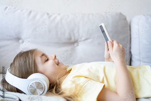 Little girl with mobile phone listening to music while lying on sofa.