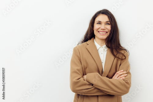 a beautiful pleasant woman in a stylish coat and well-groomed hair stands on a light background with an empty space for text with her arms folded on her chest
