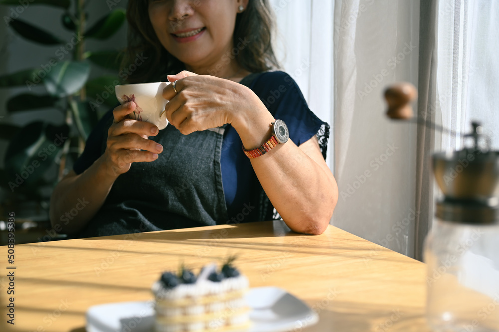 Satisfied mature woman holding a cup of coffee, relaxing, enjoying free time, weekend at home Satisfied mature woman holding a cup of coffee, relaxing, enjoying free time, weekend at home