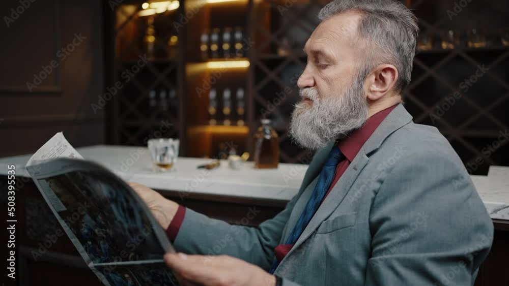 Tranquil senior bearded man reading newspaper, relaxing at home bar counter with whiskey, empty space Tranquil senior bearded man reading newspaper, relaxing at home bar counter with whiskey, empty space