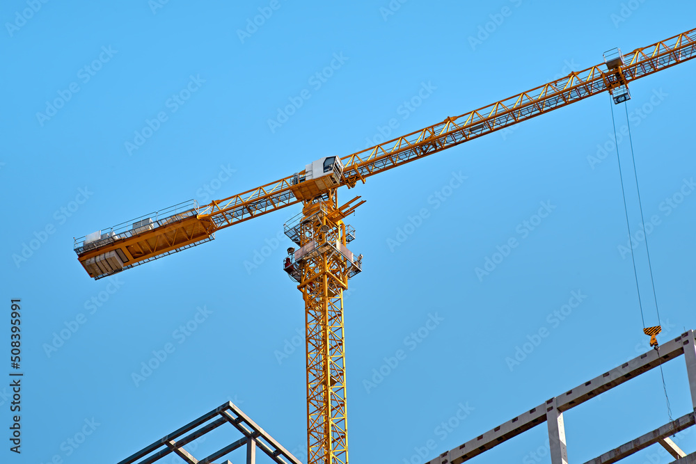 Top of yellow tower crane on skyscraper construction against clear blue sky, bottom view Top of yellow tower crane on skyscraper construction against clear blue sky, bottom view