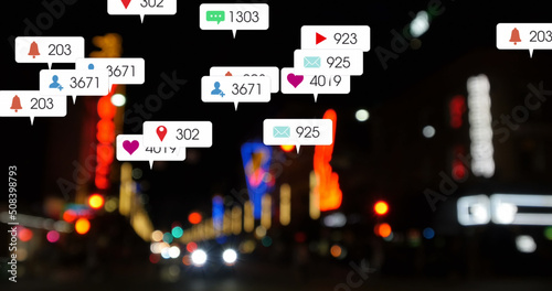 Image of social media icons and numbers over out of focus city and traffic lights