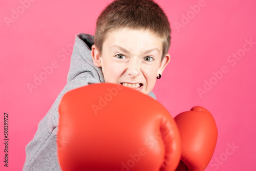 Boxer boy giving a punch with boxing gloves. Aggressive child looking at camera isolated on pink background © Egoitz