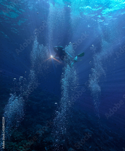 Underwater photography of a scuba diver in the deep blue sea in beautiful light and surrounded by air bubbles.