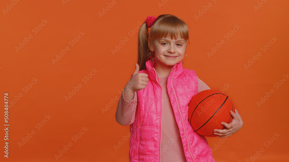 Girl sportsman basketball fan holding ball looking at camera, training dribbling. Workout sport motivation lifestyle concept. Young little blonde child kid isolated alone on orange studio background Girl sportsman basketball fan holding ball looking at camera, training dribbling. Workout sport motivation lifestyle concept. Young little blonde child kid isolated alone on orange studio background