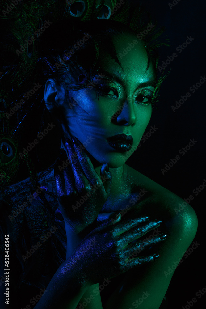 A beautiful Asian girl in a stage outfit in blue and green on a dark background.