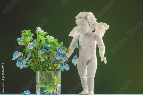 Angel baby and bouquet of blue flowers on green blurred background photo