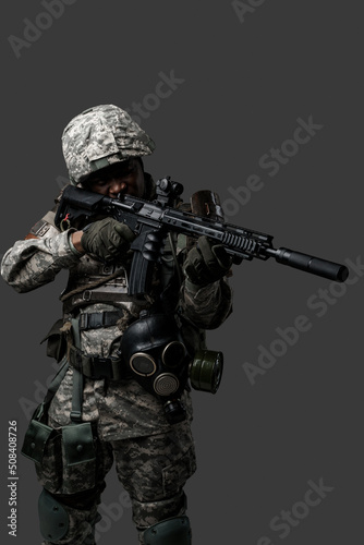 Portrait of brave army man dressed in modern camouflage uniform aiming rifle.