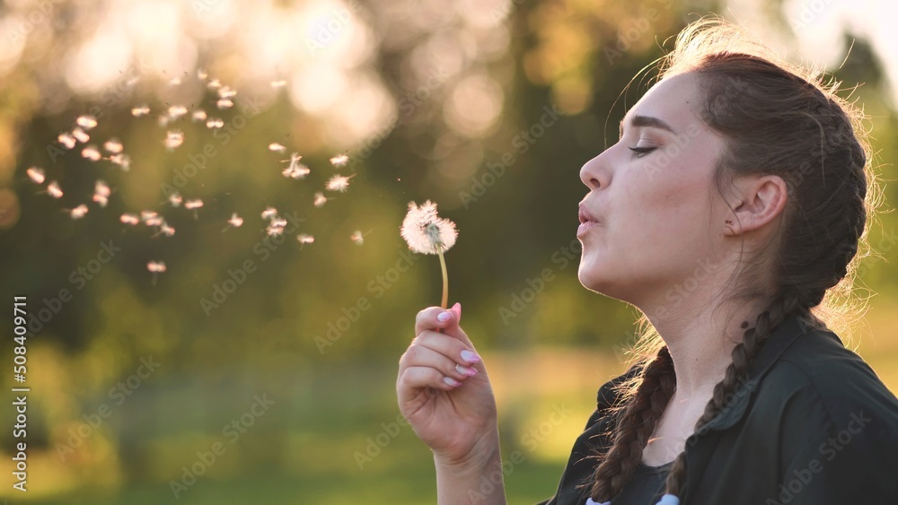 A young girl gently looks at the dandelion flower and blows it away. A young girl gently looks at the dandelion flower and blows it away.