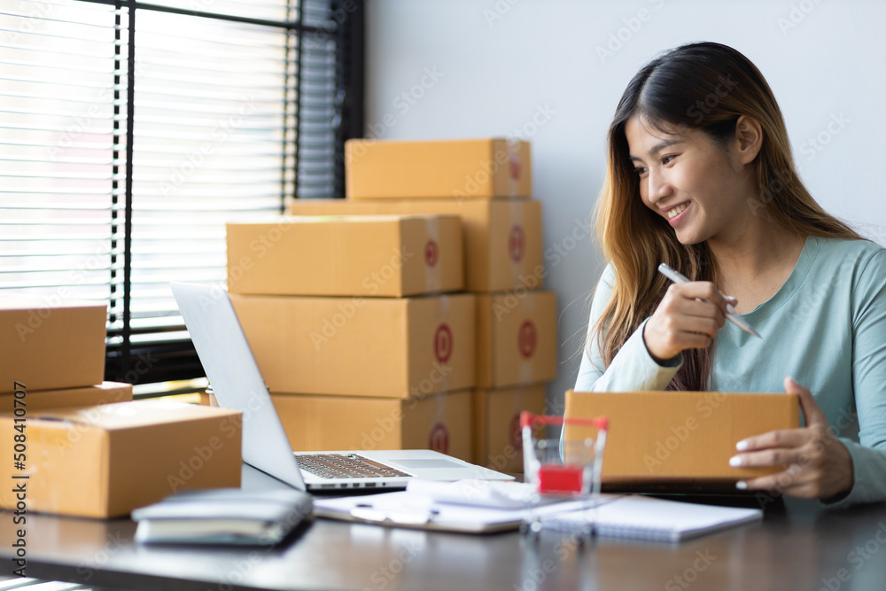 Woman running a small startup business in an office is working on a laptop and boxes for packing and preparing items for shipping. Woman running a small startup business in an office is working on a laptop and boxes for packing and preparing items for shipping.