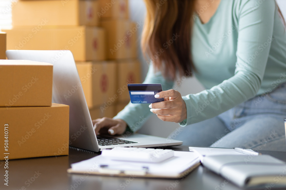 SME operators are checking the balance of online orders using their laptops. Small business entrepreneurs hold credit cards, work with laptops and boxes in the home office. Women shopping online. SME operators are checking the balance of online orders using their laptops. Small business entrepreneurs hold credit cards, work with laptops and boxes in the home office. Women shopping online.