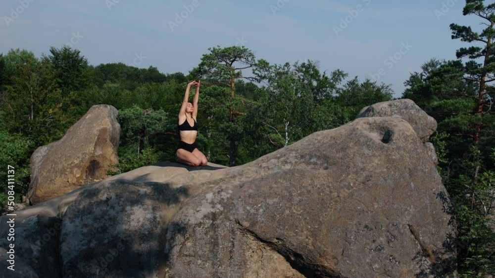 Beautiful woman is kneeling on mat playing sports, raising hands. Young beautiful sports lady training at dawn on rocky terrain. Pretty fitness girl in sportswear during workout session rocky outside Beautiful woman is kneeling on mat playing sports, raising hands. Young beautiful sports lady training at dawn on rocky terrain. Pretty fitness girl in sportswear during workout session rocky outside