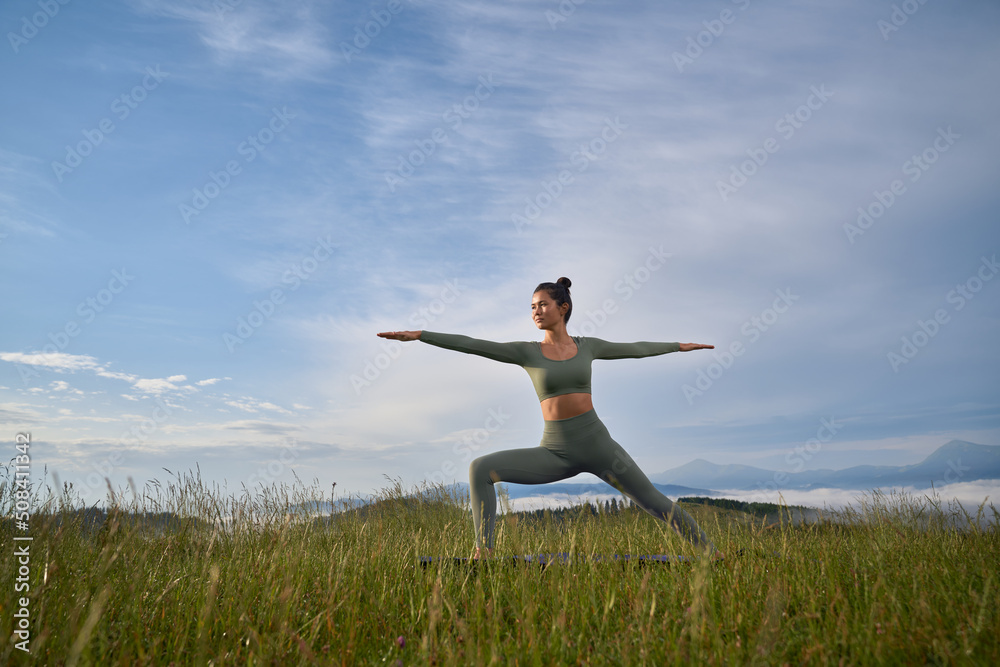 Charming woman in sport clothes doing yoga exercises among summer mountains. Pretty dark haired lady enjoying morning workout on fresh air. Charming woman in sport clothes doing yoga exercises among summer mountains. Pretty dark haired lady enjoying morning workout on fresh air.