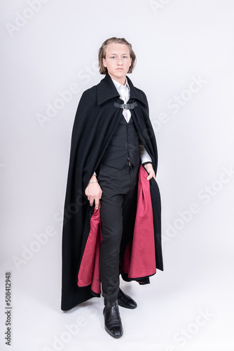 aristokratischer, junger Mann hält schwarz-roten Mantel hoch