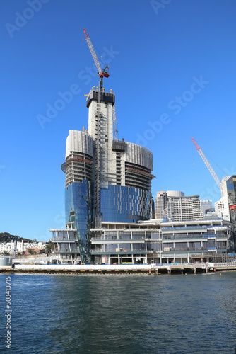 Construction of a large building in the sea bay with construction cranes against blue sky background