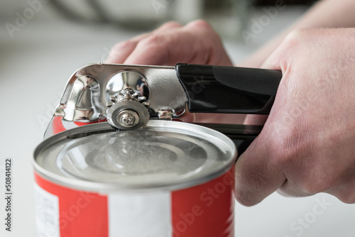 Foto Hands opening a can in a kitchen with a tin opener.