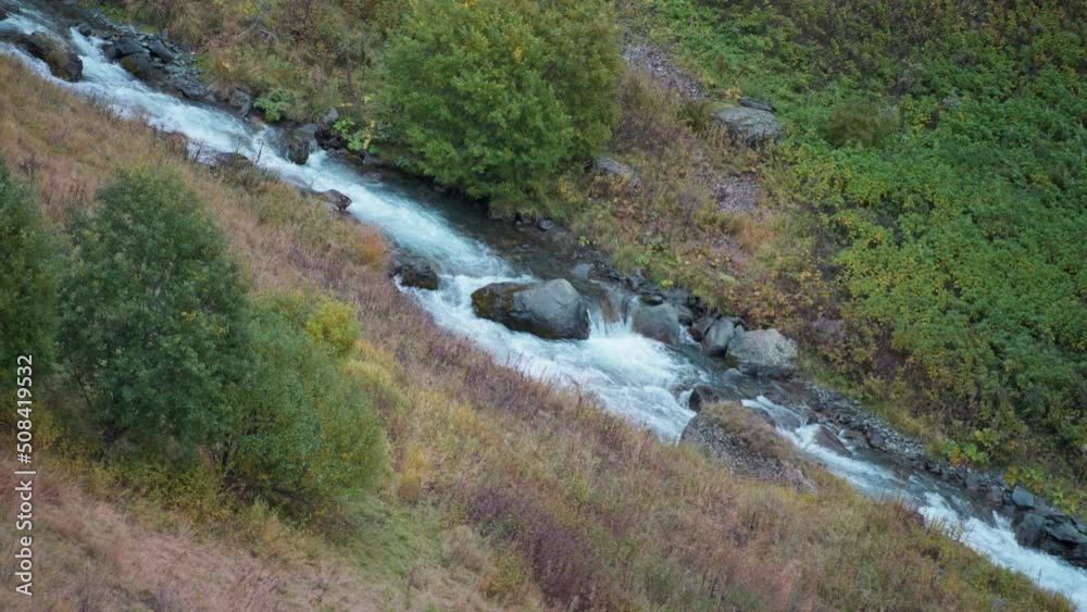 Water stream flowing smoothly in the middle of the valley in autumn. Slow motion. 