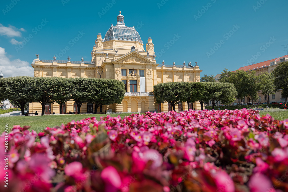 Beautiful art gallery building in central zagreb on Kralj Tomislav park on a hot summer day. Yellow building with red flowers in the foreground.
