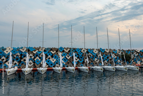 Sailing yachts moored in the bay of the seaport marina against a beautiful sky and concrete blocks.