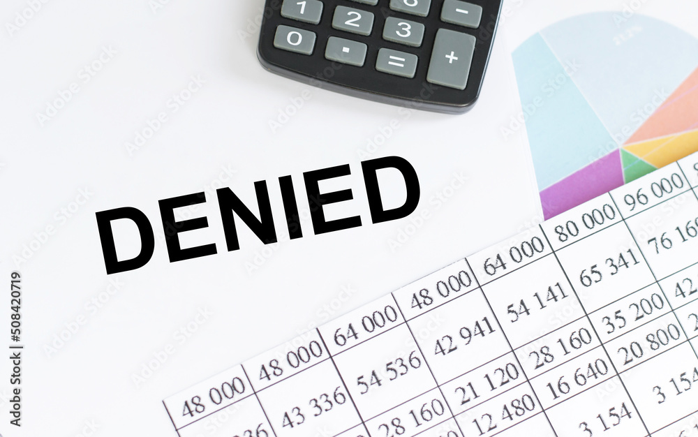 DENIED. Business concept. Notepad with text on the table next to calculator, charts and reports DENIED. Business concept. Notepad with text on the table next to calculator, charts and reports